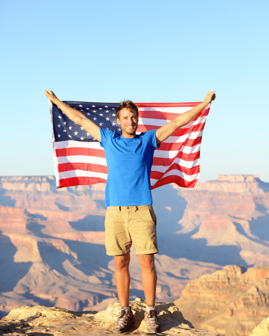 A man holding an american flag in front of the grand canyon.