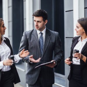 Three people in suits are standing outside talking.
