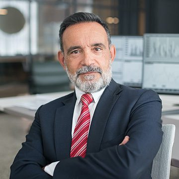 A man in suit and tie sitting at desk with arms crossed.